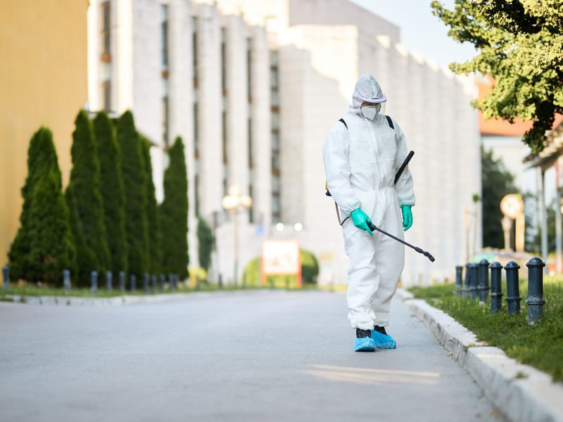 Disinfectant worker in protective suit sanitizing empty city streets during COVID-19 epidemic.